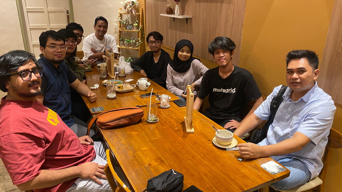 Delapan anggota Tech Voice Indonesia berkumpul mengelilingi meja kafe saat meetup komunitas.